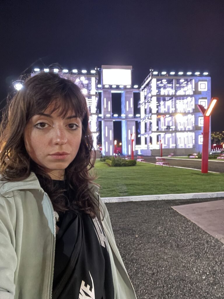 McKenzie on location at a night shoot with a lit set behind her